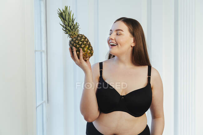 Allegro giovane modello in lingerie con ananas contro parete bianca — Foto stock