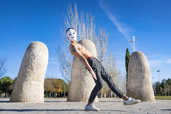 Hombre sin camisa con máscara blanca bailando mientras está de pie en el sendero - foto de stock