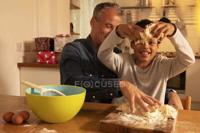 Padre e hijo amasando masa en la mesa mientras están sentados en la cocina  — Amasado, Caucásica - Stock Photo | #484389312