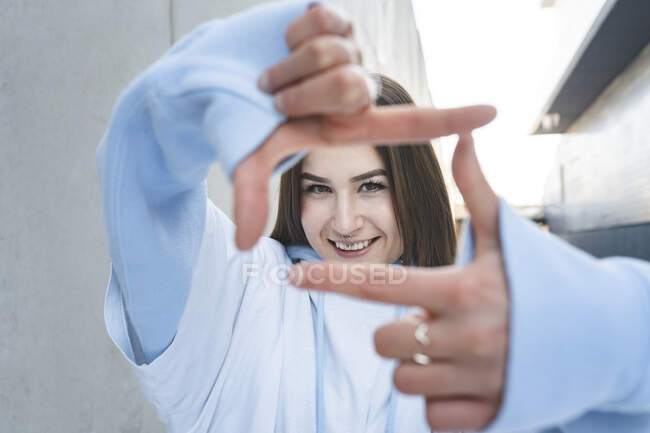 Mujer sonriendo mientras hace marco de dedo contra la pared - foto de stock