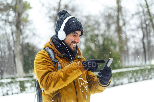 Homme utilisant un téléphone portable tout en écoutant de la musique à travers des écouteurs sur la terre enneigée pendant l'hiver — Photo de stock