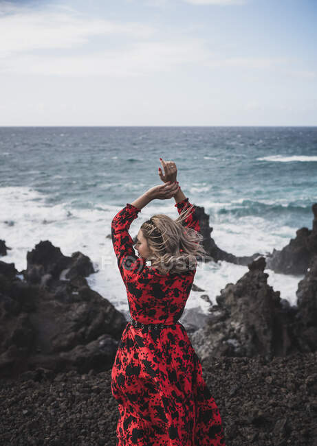 Mujer de pie con los brazos levantados contra el mar en Los Hervideros, Lanzarote, España - foto de stock