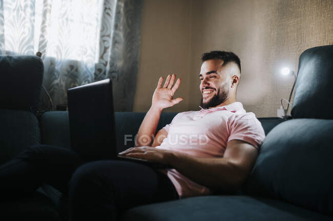 Молодий бізнесмен махає рукою по ноутбуку, сидячи на дивані у вітальні. — стокове фото