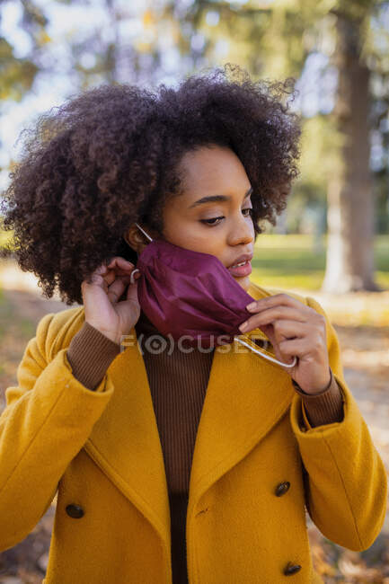 Молодая женщина снимает защитную маску, стоя в парке — стоковое фото