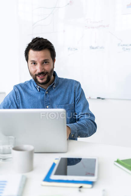 Porträt eines lächelnden Mannes mit Laptop im Büro — Stockfoto
