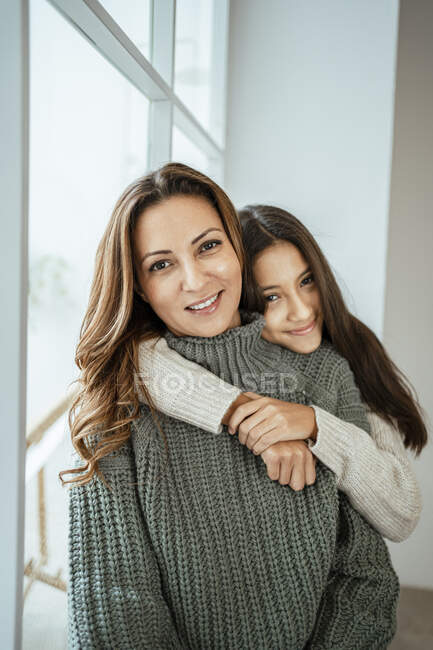 Улыбающаяся девушка обнимает мать, сидя дома — стоковое фото