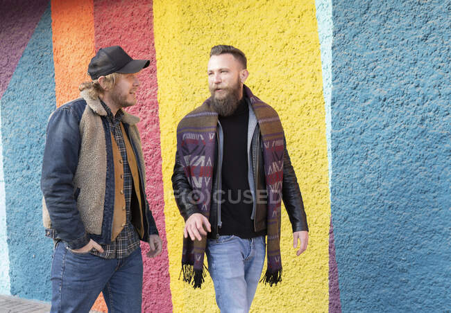 Gay copains parler tout en marchant contre coloré mur dans ville — Photo de stock