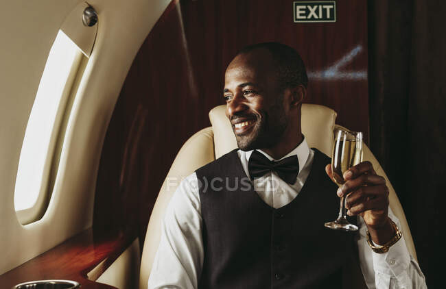 Empreendedor masculino sorridente segurando champanhe olhando pela janela no avião — Fotografia de Stock
