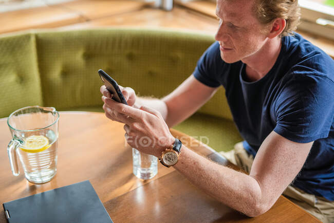 Mensajería de texto de hombre adulto medio en el teléfono móvil en la sala de estar - foto de stock