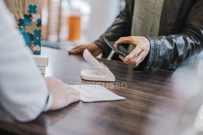 Midsection of customer with mobile phone at checkout counter in chemist shop — Stock Photo