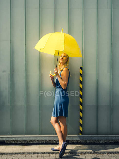 Mujer joven con paraguas en el sendero contra la pared durante el día soleado - foto de stock