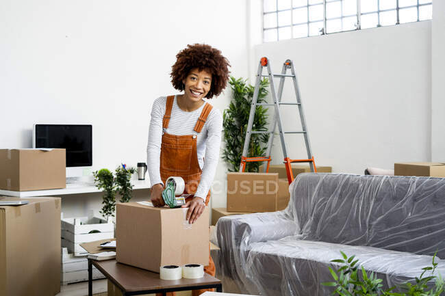 Щаслива молода жінка упаковує картонну коробку під час переїзду в новій квартирі — стокове фото