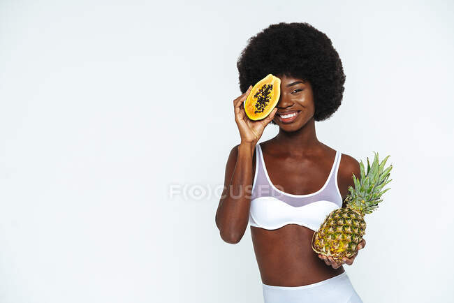 Afro giovane donna che indossa lingerie tenendo papaia e ananas sullo sfondo bianco — Foto stock