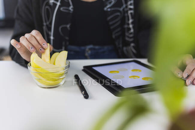 Junge Designerin mit digitalem Tablet und Apfel bei der Arbeit im Studio — Stockfoto