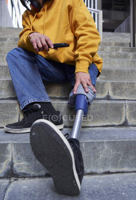 Homme handicapé avec prothèse de jambe tenant le téléphone intelligent tout en étant assis sur les marches — Photo de stock