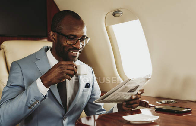 Lächelnder Geschäftsmann liest Zeitung beim Kaffee im Flugzeug — Stockfoto