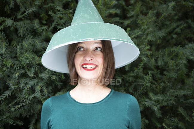 Mujer feliz con pantalla de lámpara en la cabeza contra la planta - foto de stock