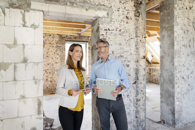 Mujer de negocios sonriente con tableta digital mirando hacia otro lado mientras está de pie por colega en el sitio de construcción - foto de stock