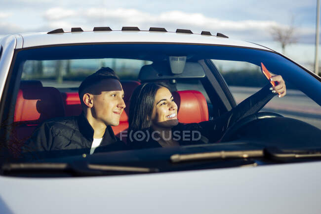 Sorrindo namorada tirando selfie com namorado através do telefone celular enquanto sentado no carro — Fotografia de Stock