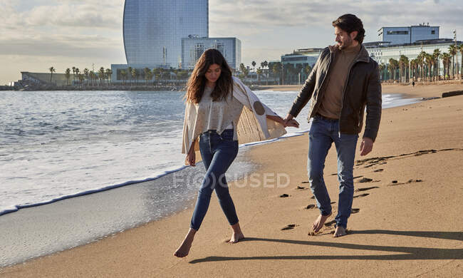 Young man holding hand on woman while walking on beach — Stock Photo