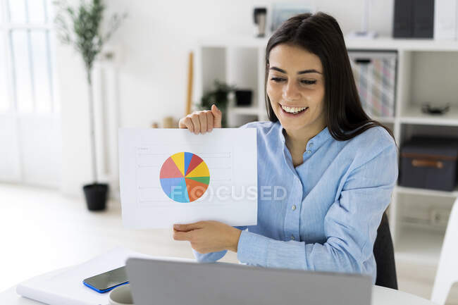 Empresario mostrando gráfico de pastel de negocios a la computadora portátil de llamada de conferencia mientras trabaja en la oficina - foto de stock