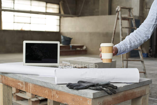 Hand of male architect placing coffee cup on table in building — Stock Photo