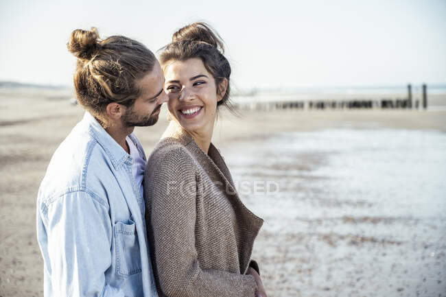 Petite amie souriante regardant petit ami tout en se tenant à la plage — Photo de stock