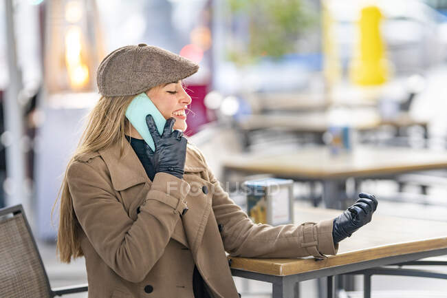 Smiling woman talking on smart phone at sidewalk cafe — Stock Photo