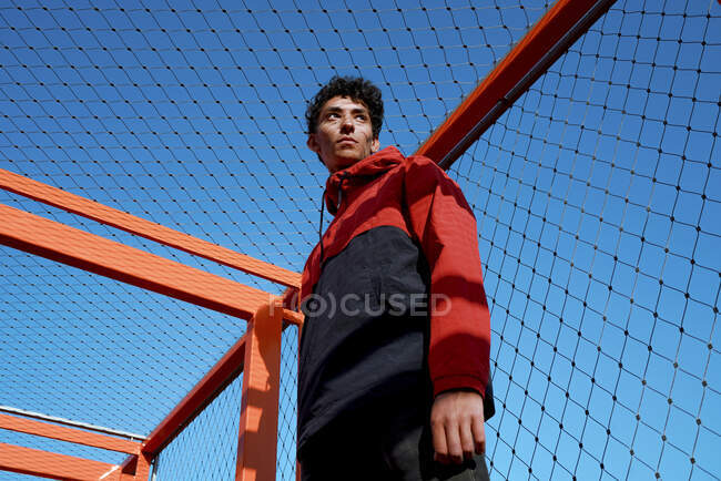 Ragazzo premuroso in piedi sotto la recinzione contro il cielo blu chiaro — Foto stock