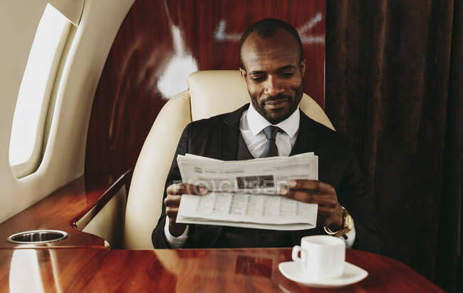 Jeune homme d'affaires lisant un journal en avion — Photo de stock