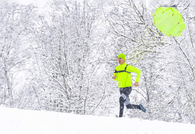 Спортсмен с парашютом, бегущий по снегу в лесу зимой — стоковое фото