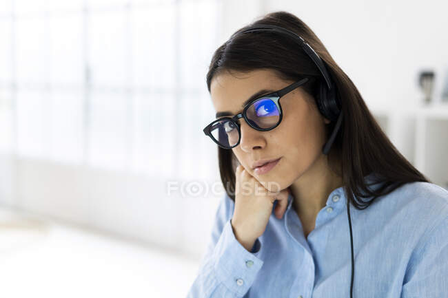 Бізнес-леді в мікрофонній гарнітурі та окулярах дивиться, сидячи в офісі — стокове фото