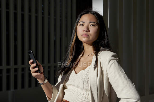 Betrachtet junge Frau mit Smartphone, während sie sich an sonnigem Tag an Tor lehnt — Stockfoto