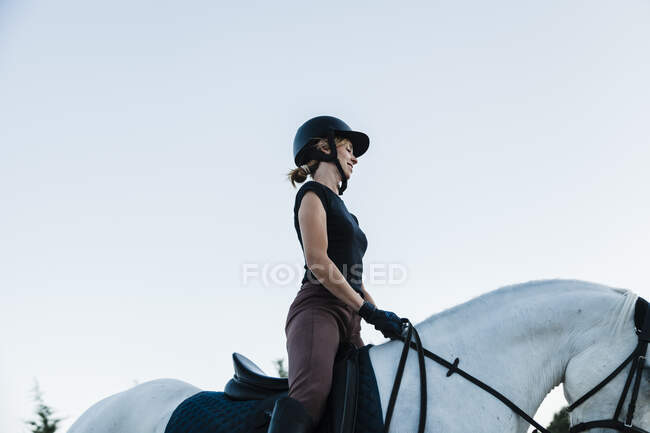 Mujer usando ropa de cabeza caballo a caballo contra el cielo despejado - foto de stock