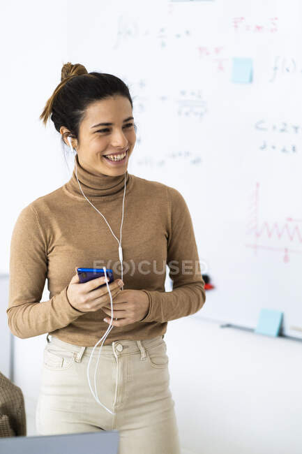 Estudiante riendo mientras habla por teléfono inteligente en la sala de estar - foto de stock