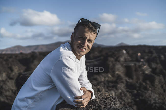 Lächelnder männlicher Tourist lehnt an Vulkangestein während eines sonnigen Tages in Los Hervideros, Lanzarote, Spanien — Stockfoto