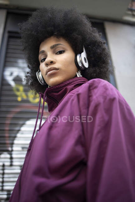 Mujer joven y segura con auriculares de pie contra el hierro corrugado - foto de stock