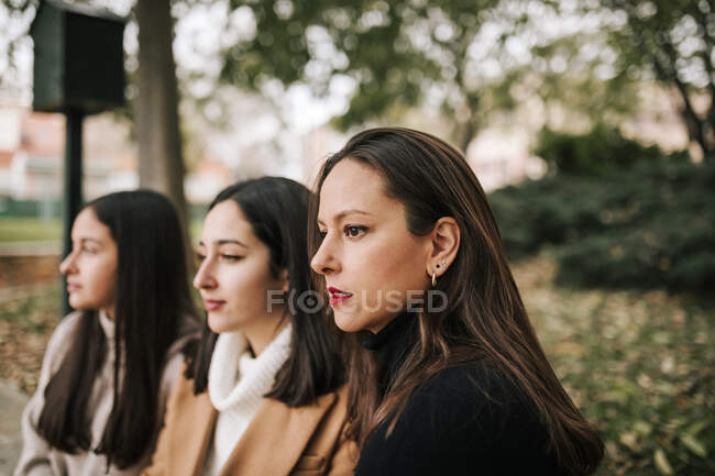 Духовна мати й доньки відвернулися, сидячи в парку. — стокове фото