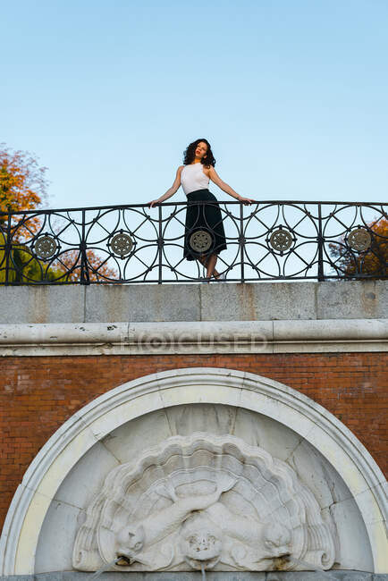Молода жінка позує, стоячи на мосту біля чистого неба в парку — стокове фото