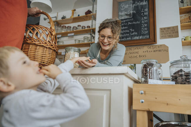 Mujer emprendedora sonriente dándole un capricho a un niño en una tienda de residuos cero - foto de stock