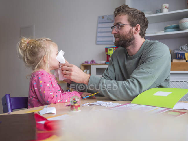Padre giocoso che tiene la carta sulla figlia mentre si siede a tavola — Foto stock