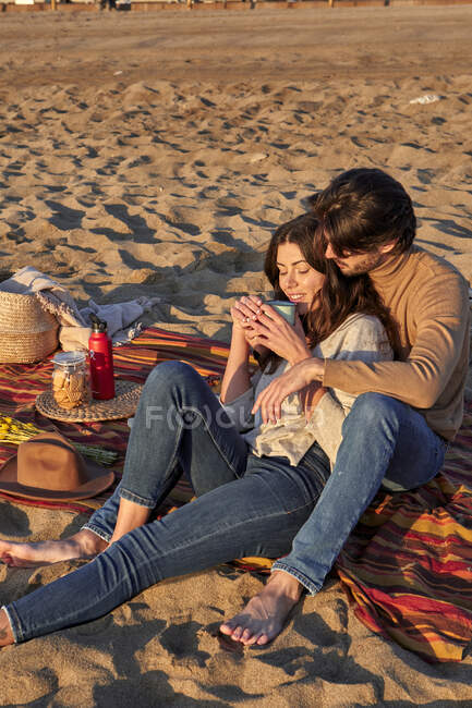 Fidanzata bere caffè mentre appoggiato sul fidanzato in spiaggia — Foto stock