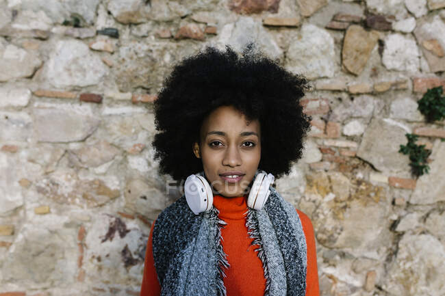 Junge Frau mit Kopfhörern in warmer Kleidung gegen Steinmauer — Stockfoto