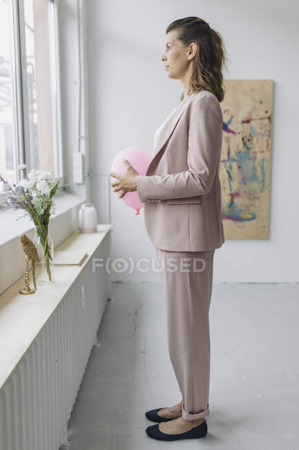 Businesswoman holding balloon in front of stomach in office — Stock Photo