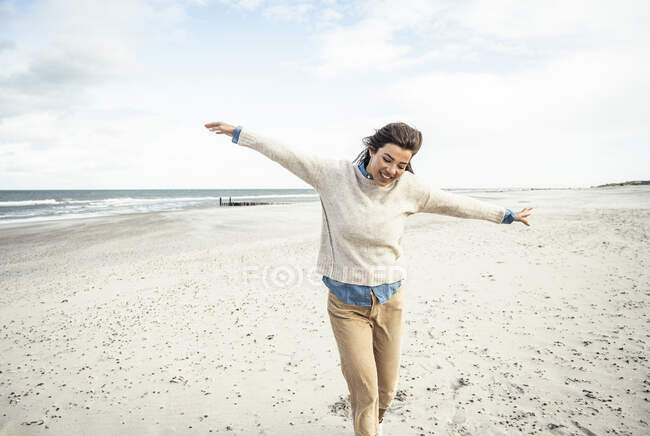 Портрет молодої жінки, що йде на піщаному пляжі з піднятими руками — стокове фото