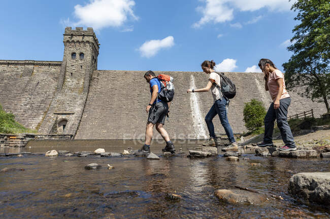 Caminhantes masculinos e femininos caminhando em pedra sobre a água durante as férias — Fotografia de Stock