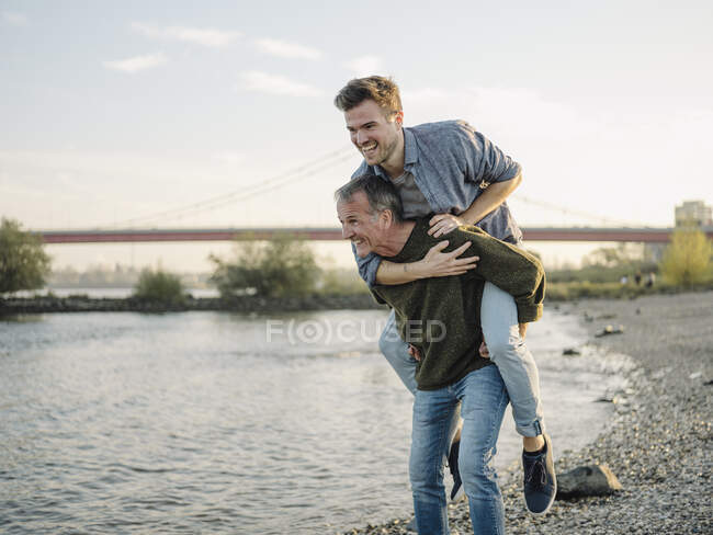Happy father giving piggyback ride to son at riverbank — Stock Photo
