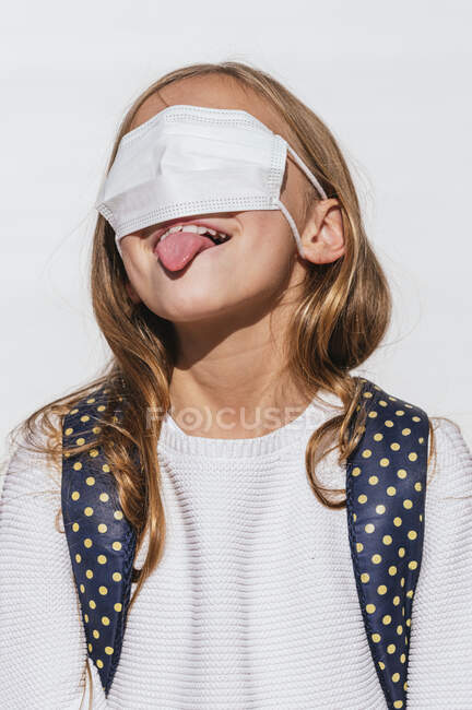 Verspieltes Mädchen, das während COVID-19 die Zunge herausstreckt, während es die Augen mit einer schützenden Gesichtsmaske bedeckt — Stockfoto