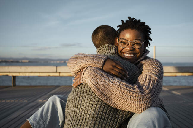 Happy woman embracing friend while sitting on footpath during sunset — Stock Photo