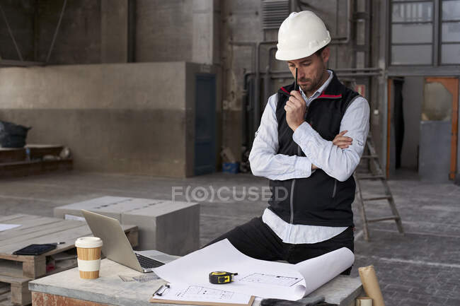 Architetto maschio pensando mentre analizza cianografia sul tavolo in costruzione — Foto stock